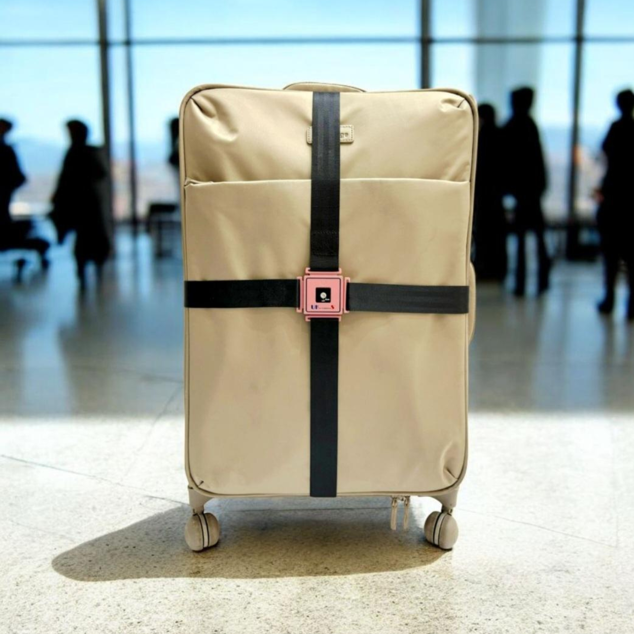 Beige suitcase with a black strap and pink buckle in an airport setting